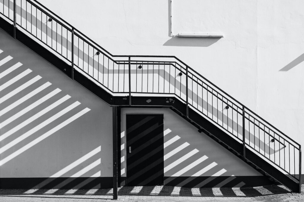 An outside staircase casts shadows on the wall and the paved floor - in black and white.