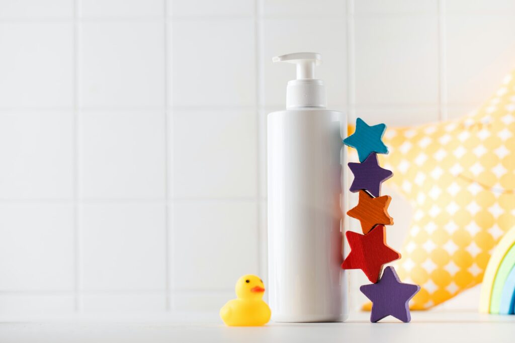 Blank bottle of baby skincare product and small toys stand on table in bathroom