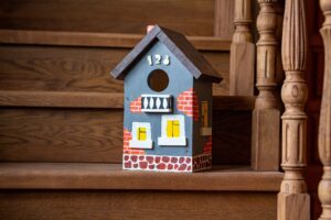 A hand-painted vibrant birdhouse close-up stands on the wooden staircase of a house.