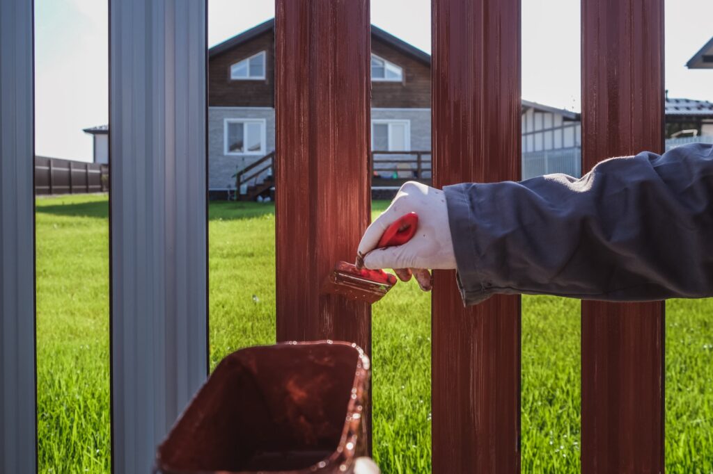 A man paints an iron fence in the garden