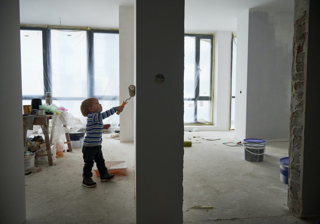 Adorable baby boy painting wall in apartment.