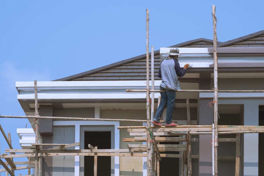 Asian builder worker on wooden scaffolding is painting roof structure of modern house