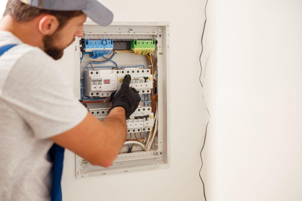 Electrical technician in uniform looking focused while working in a switchboard with fuses