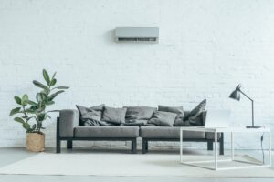 empty room with grey sofa, ficus, laptop on table and air conditioner on white wall