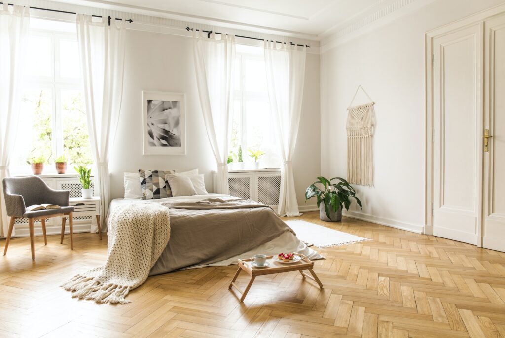 Grey armchair next to bed with blanket in bright bedroom interio