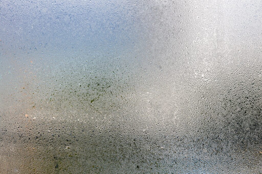 Misted glass, silver rain drops dew drops on transparent glass window.