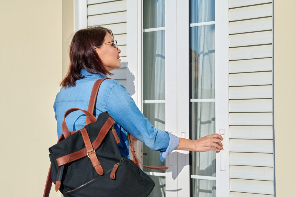 Woman with backpack opening shutters outside doors on window