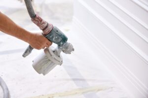 Worker painting wall with spray gun in white color.