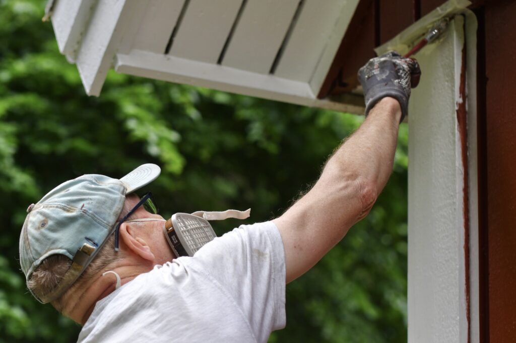 A man painting house exterior with white color