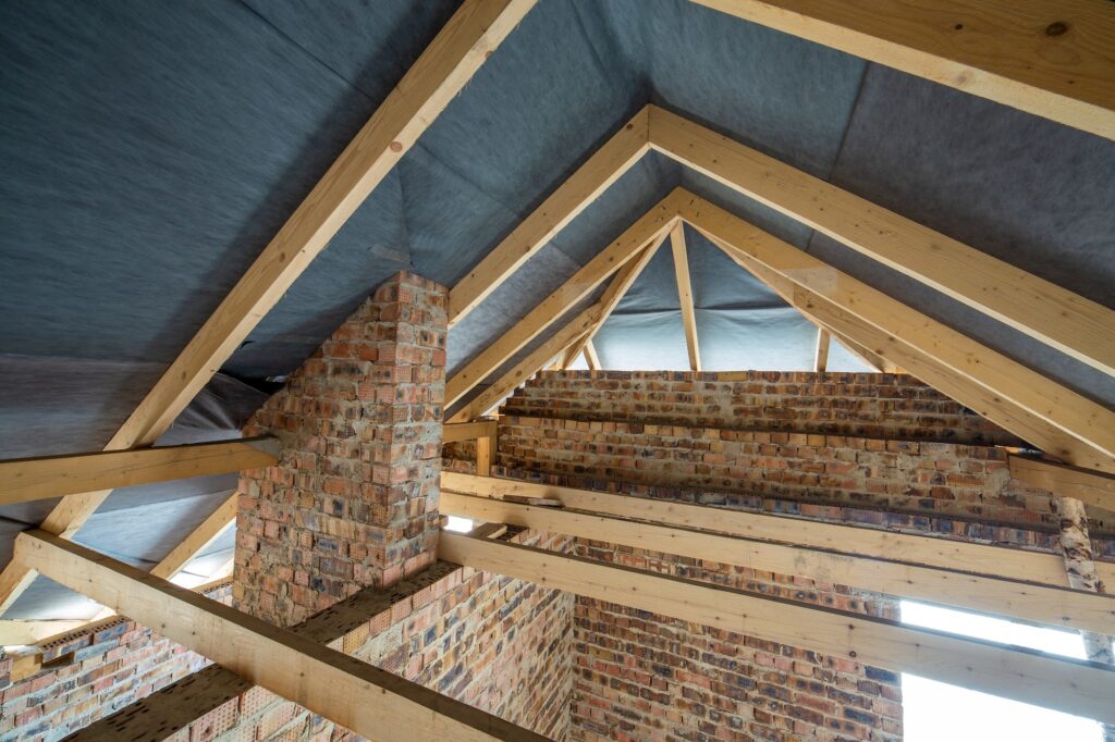 Attic space of a building under construction with wooden beams of a roof structure and brick walls