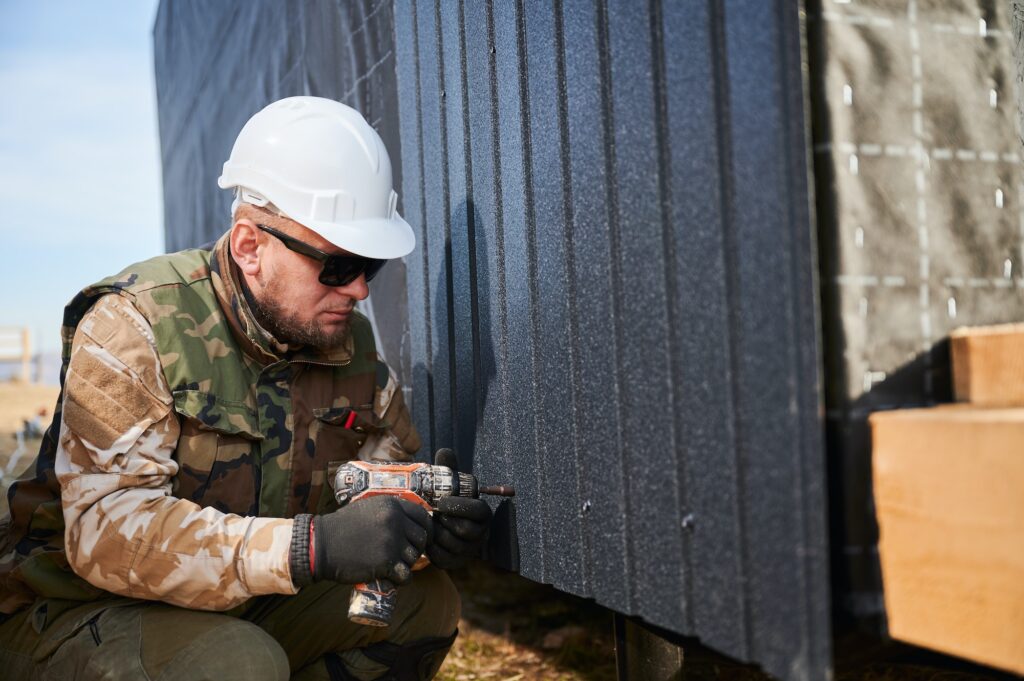 Builder installing corrugated iron sheet used as facade of future wooden frame house.