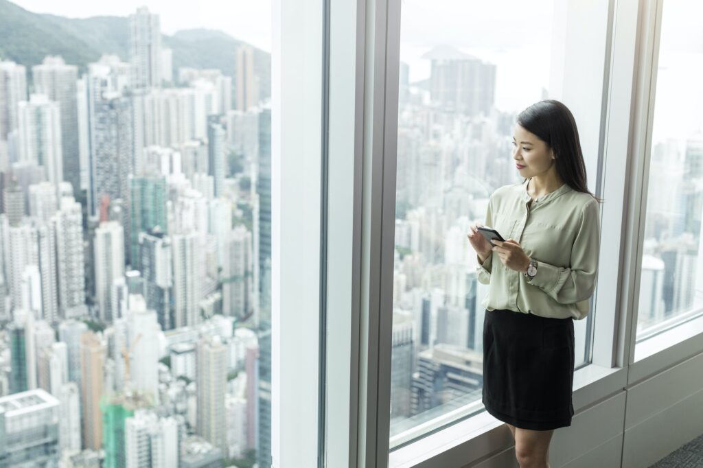 Businesswoman with smartphone looking out of window