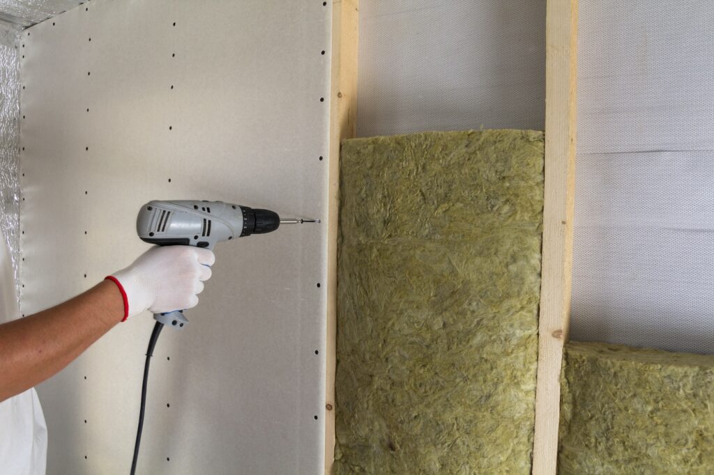 Close-up of worker hand with electric screwdriver fastening drywall to wooden timber frame with