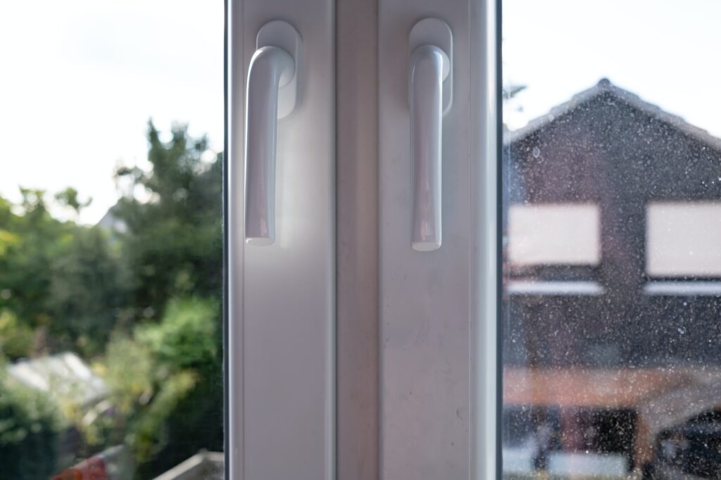 Closed white PVC window with two sashes, with dirty glass, through which the courtyard is visible
