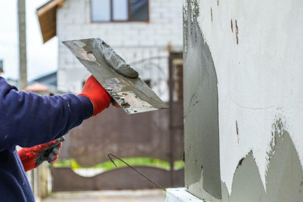 Construction worker covering house wall with adhesive cement glue