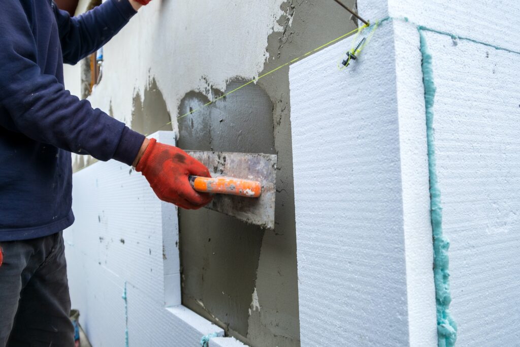 Construction worker installing styrofoam insulation sheets on house facade wall