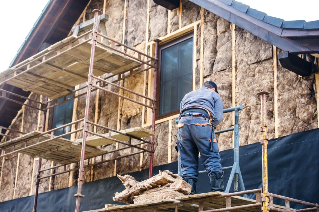 Construction worker thermally insulating house facade with glass wool.