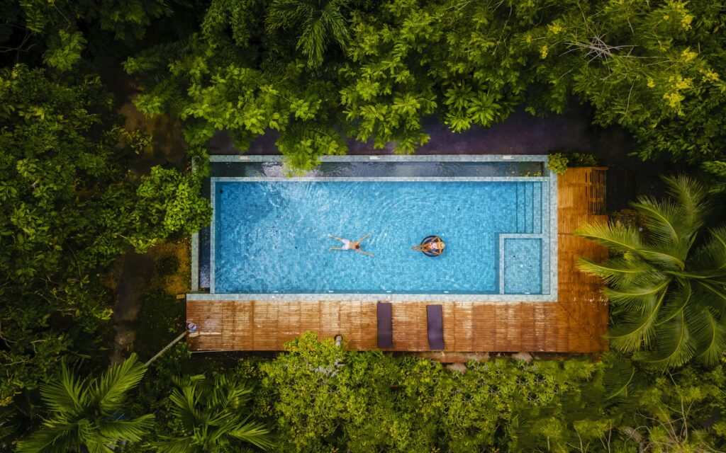 couple men and woman in swimming pool in the jungle of Krabi Thailand, aerial view with drone above