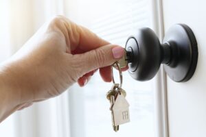 Female inserting house keys into a doorknob lock of a front door of a home.