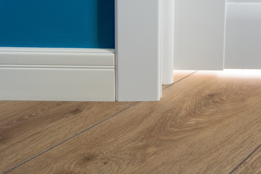 Laminated parquet floors immitating oak texture, white baseboard, white door