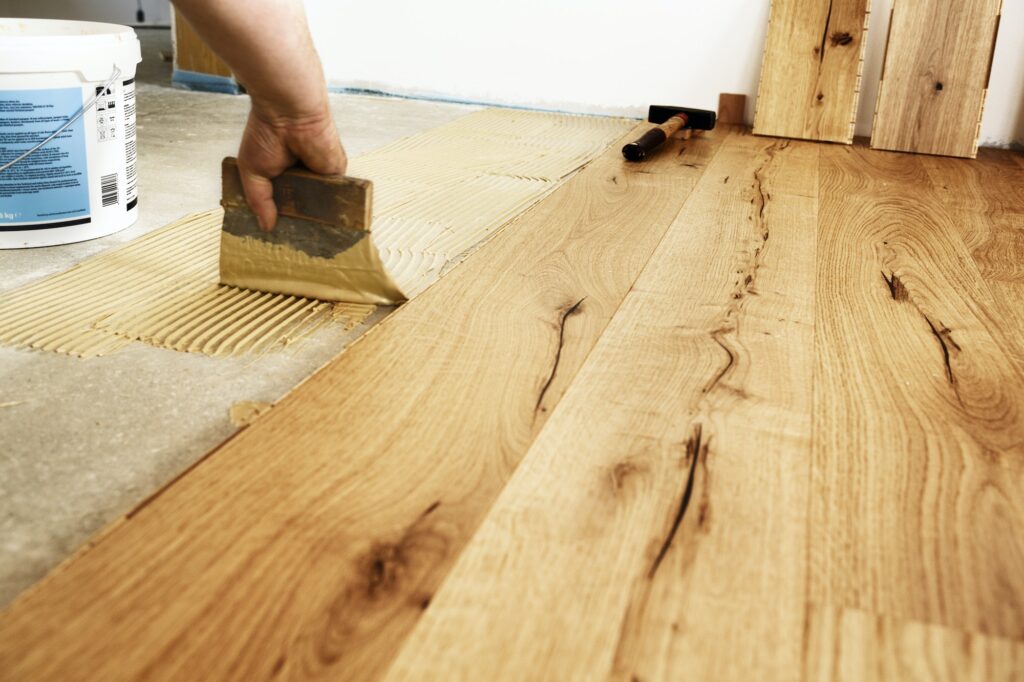 Man applying glue for laying finished parquet flooring, close-up