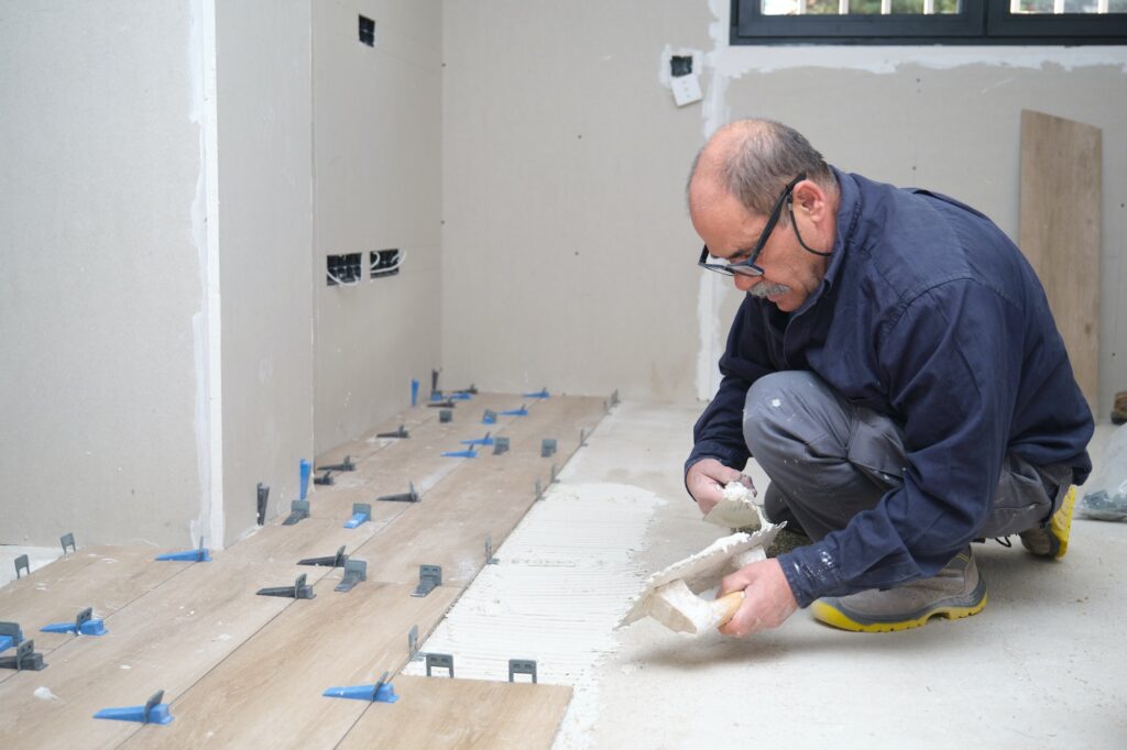 Tiler putting tiles adhesive to the floor with the trowel and notched trowel.