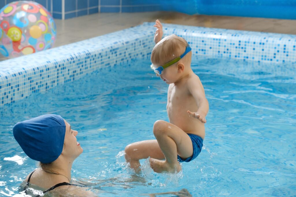 Toddler child trained to swim in indoor swimming pool