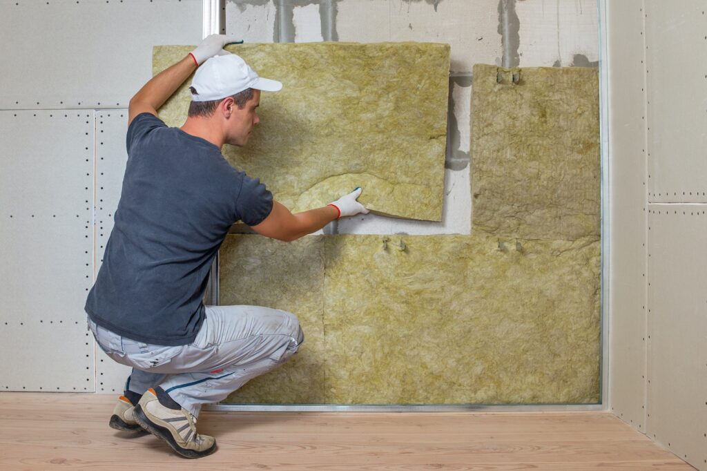 Worker insulating a room wall with mineral rock wool thermal insulation